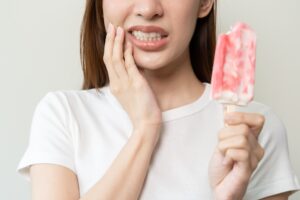 woman hold her cheek after experiencing tooth sensitivity from a popsicle
